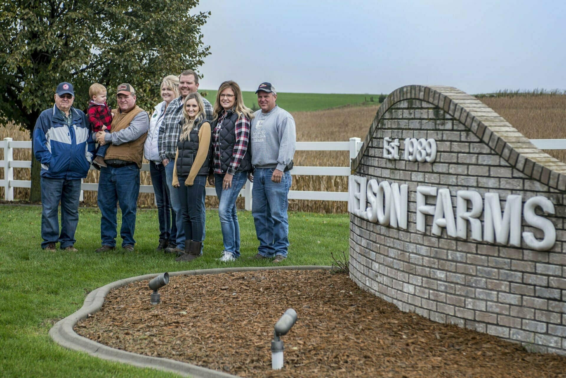 The Nelson family stands by their Nelson Farms sign next to a cornfield.