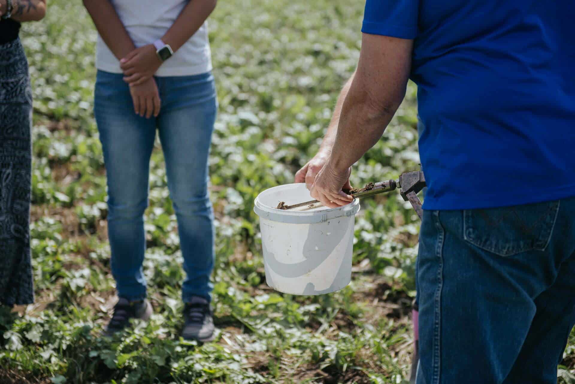 A farmer places soil samples in a bucket.