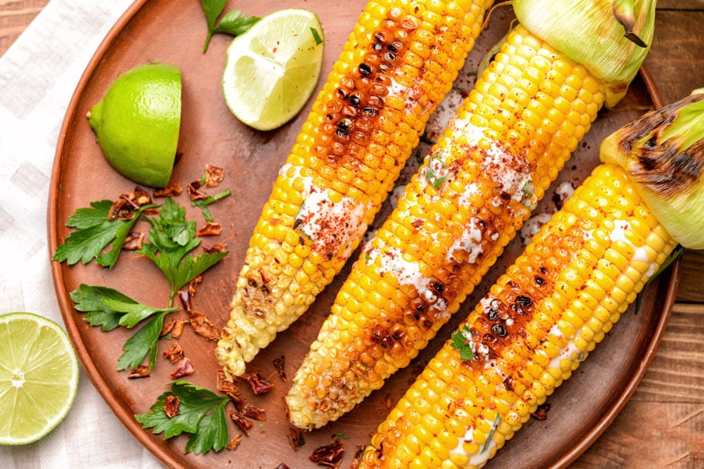 Fried corn on the cob next to cut limes on a plate