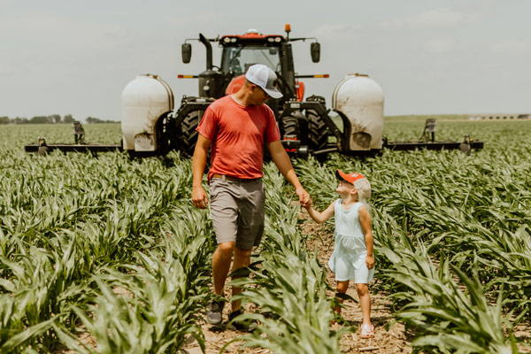 Farmer holding his daughter's hand in front of combine in corn field