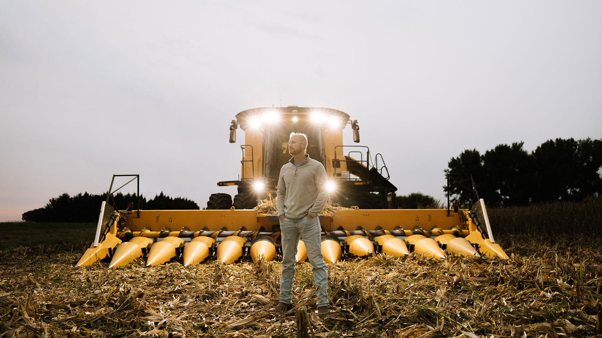Man standing in front of farm machinery at dusk